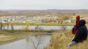 Two people overlook the Oceti Sakowin Camp on Standing Rock Sioux treaty territory in Cannonball, North Dakota. This photo is a production still from the upcoming documentary 'Layin' the Pipe' by Caitlin Kazepis. Photo by Caitlin Kazepis.