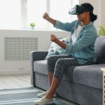 A person wearing a VR headset, sitting on a couch and interacting with the virtual environment