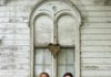 Two musicians standing with an acoustic guitar in front of a weathered white building