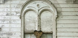Two musicians standing with an acoustic guitar in front of a weathered white building