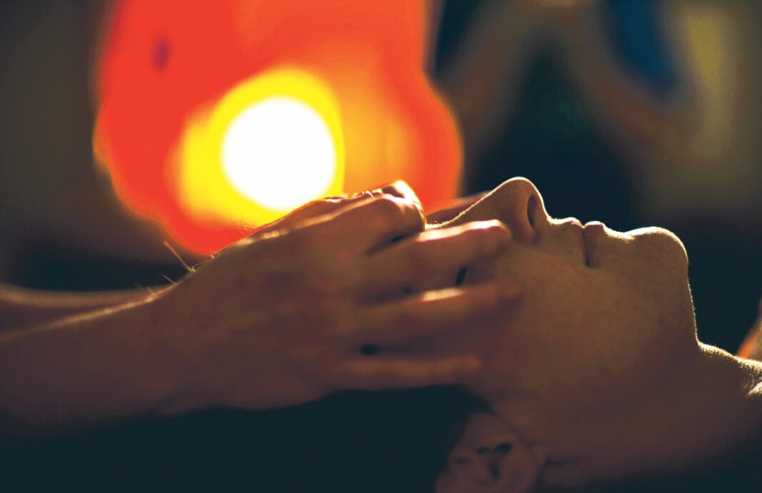 Person with eyes closed receiving a facial massage.
