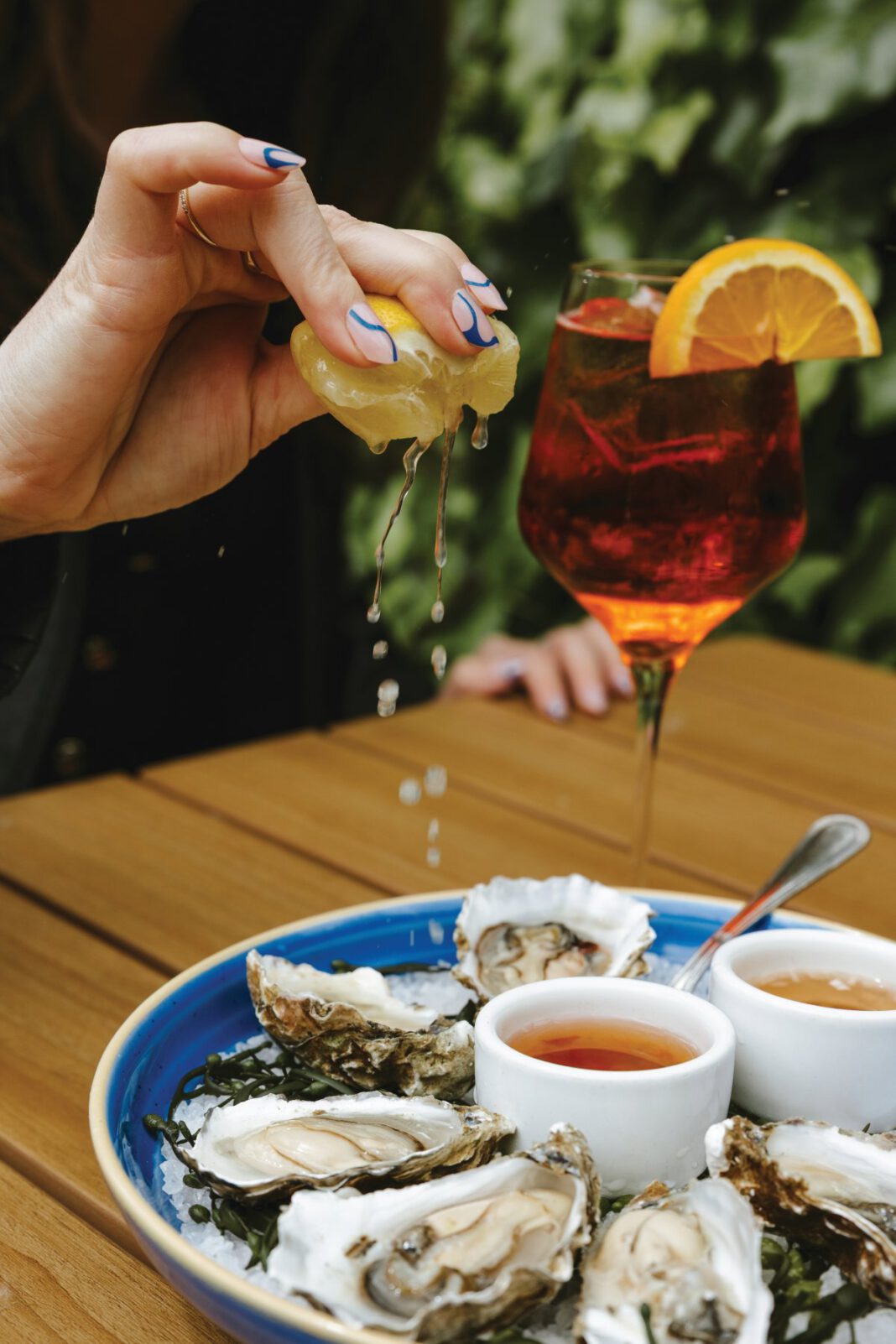 A plate of fresh oysters on a table with a woman squeezing a lemon over them.