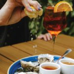 A plate of fresh oysters on a table with a woman squeezing a lemon over them.