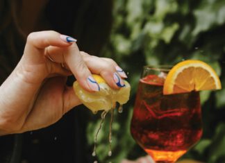 A plate of fresh oysters on a table with a woman squeezing a lemon over them.