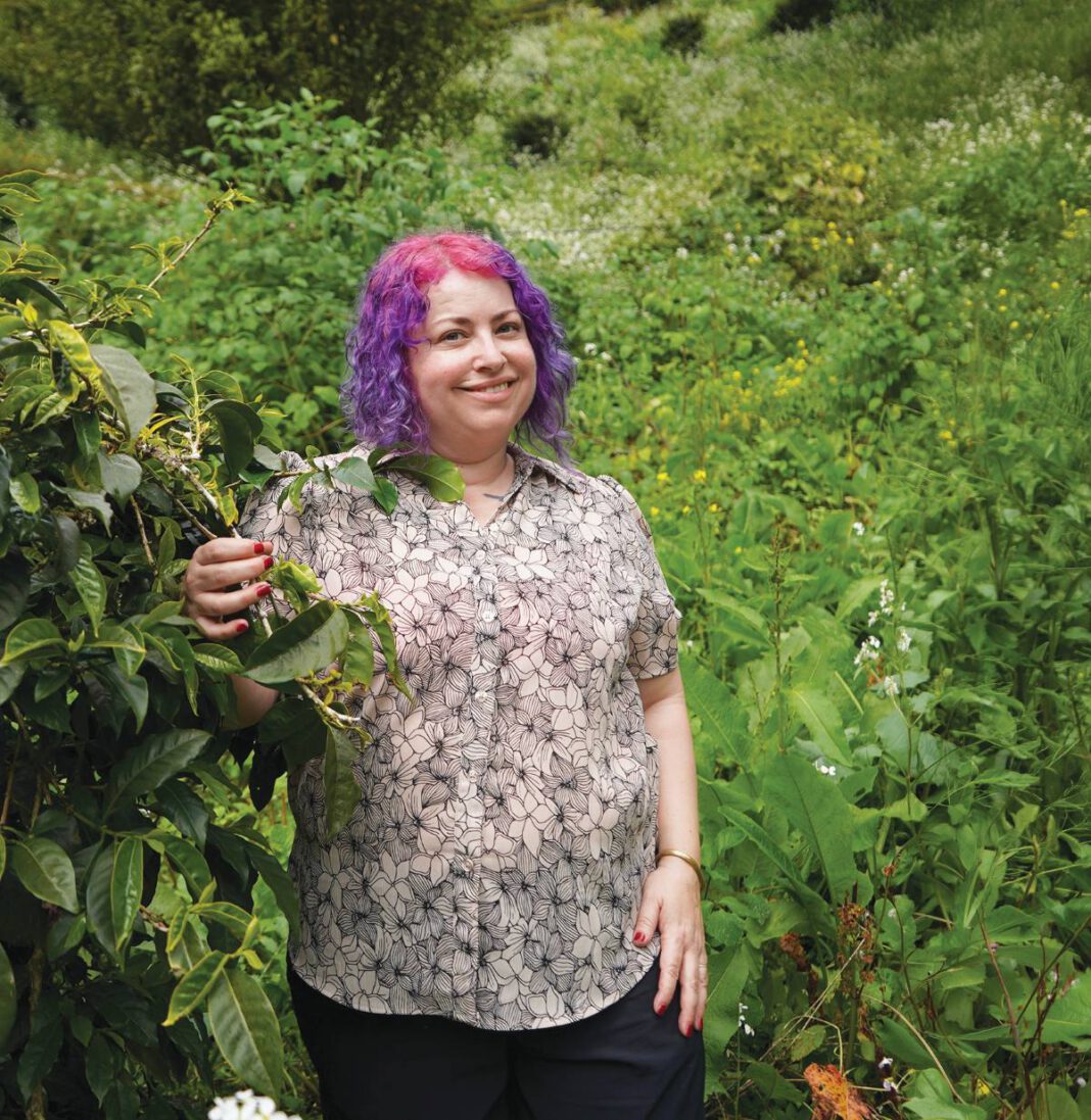 Devorah Freudiger standing in front of green shrubbery.
