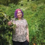 Daily Grind: Devorah Freudiger’s Coffee Connection Devorah Freudiger standing in front of green shrubbery.