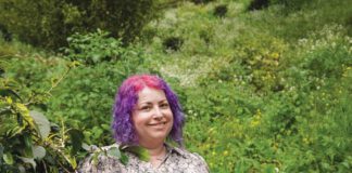 Devorah Freudiger standing in front of green shrubbery.