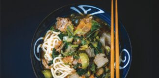 Bowl of noodles with vegetables and meat served with chopsticks