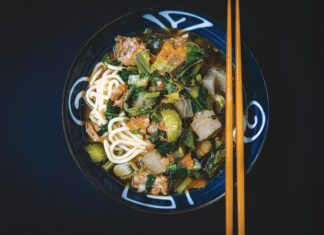 Bowl of noodles with vegetables and meat served with chopsticks
