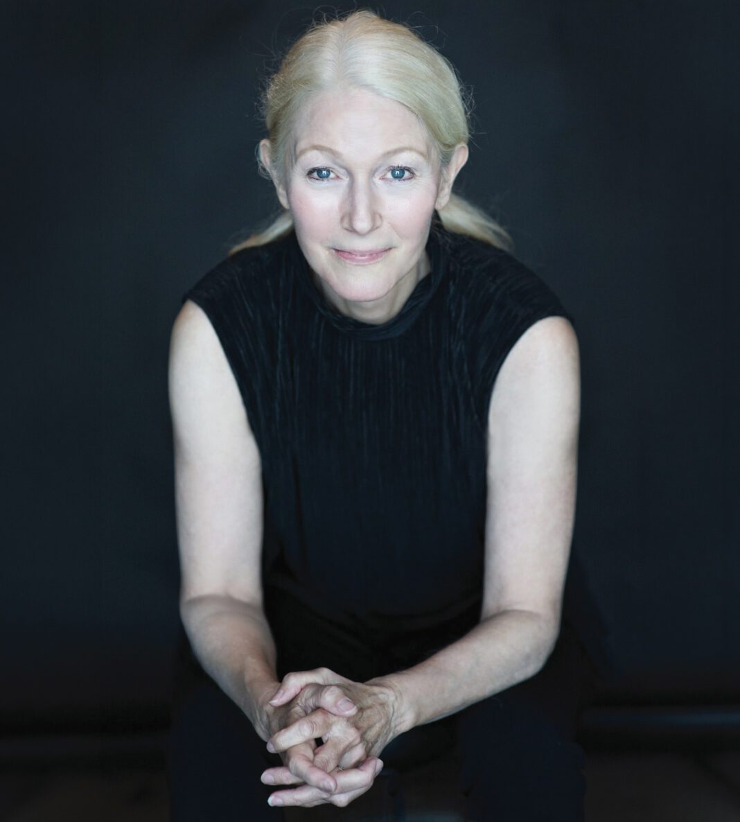 Marin author Nina Schuyler against a black background, with her blond hair pulled back and wearing a black sleeveless top.