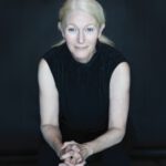 The Rippling of Rivers: ‘Open the Floodgates’ Gives Voice to a Waterway Marin author Nina Schuyler against a black background, with her blond hair pulled back and wearing a black sleeveless top.