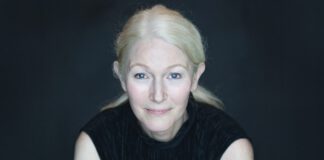 Marin author Nina Schuyler against a black background, with her blond hair pulled back and wearing a black sleeveless top.