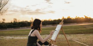 Artist painting on a canvas outdoors beside an easel at sunset