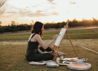 Artist painting on a canvas outdoors beside an easel at sunset