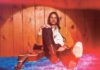 Duane Betts sits on a blue carpet next to a guitar.