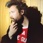 Father John Misty in a red shirt and black jacket.