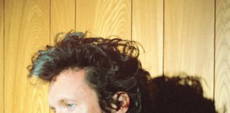 Father John Misty in a red shirt and black jacket.