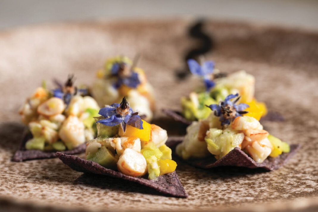 Pink shrimp ceviche with diced mango served on two blue corn tortilla chips.