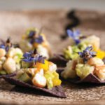 Pink shrimp ceviche with diced mango served on two blue corn tortilla chips.