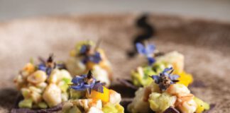 Pink shrimp ceviche with diced mango served on two blue corn tortilla chips.