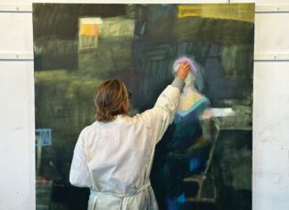 Art in the Act: ICB/ART Shows Artists at Work An artist in a paint-splattered smock reaches up to add paint to a large abstract portrait on canvas.