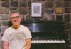In the Mix, New Book Decodes Music Producing A smiling man in glasses and a graphic T-shirt stands in front of a Steinway upright piano against a stone wall.