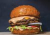 A double-patty cheeseburger with melted cheese, pink sauce, lettuce, tomato, pickles and onion on a sesame bun.