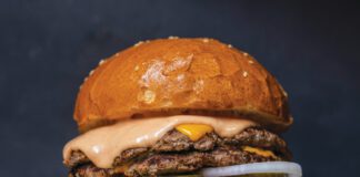 A double-patty cheeseburger with melted cheese, pink sauce, lettuce, tomato, pickles and onion on a sesame bun.