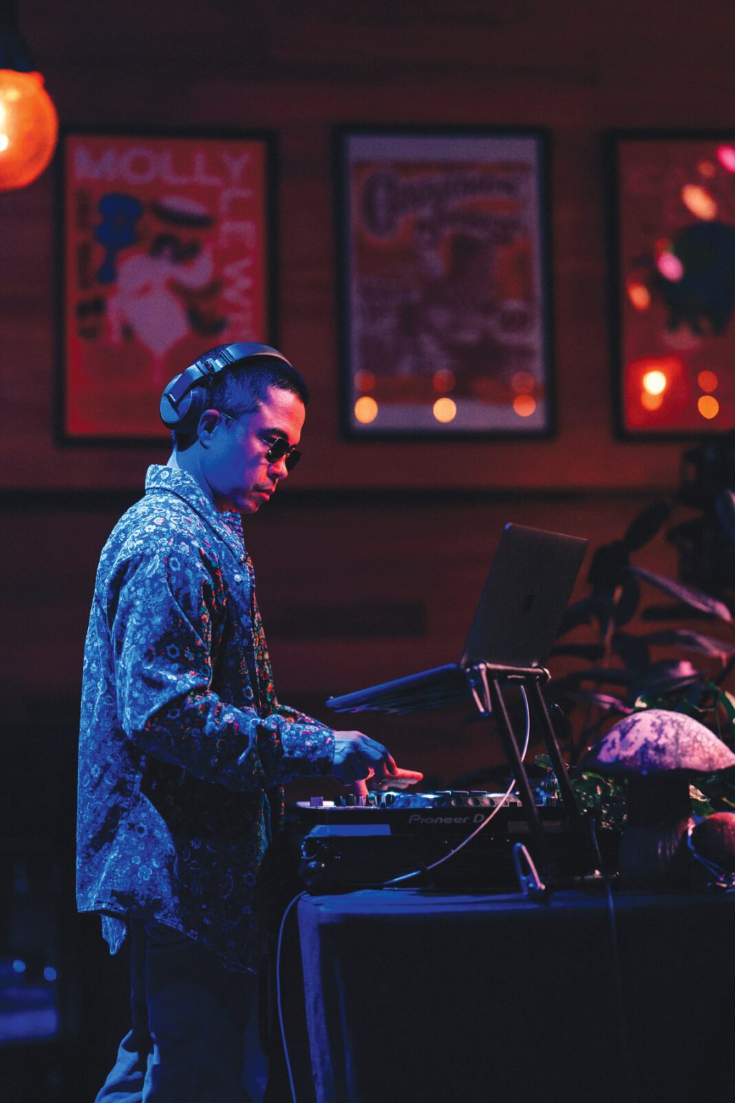 A man in headphones, sunglasses and a patterned shirt works the DJ controls.