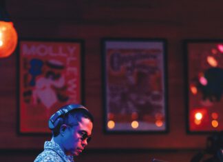 A man in headphones, sunglasses and a patterned shirt works the DJ controls.