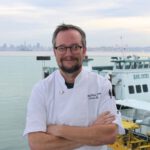 Regionality Reigns: Chris Ball Plans Perfect Last Meal A smiling man with graying hair, eyeglasses and a beard stands with his arms crossed wearing a white chef’s coat.