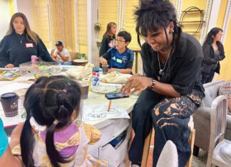 Saturday Friends: The Kove Brings San Rafael Neighbors Together A young woman with spiky black hair, braids and piercings sitting at a table, laughing with a little girl seen from behind.