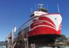 A red and white boat named Harbor Queen sits out of the water in a boatyard, surrounded by scaffolding and ladders.