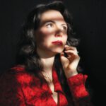 Dramatic Pause : ‘Betrayal’ Comes to Marin Theatre A woman with long dark hair and red lipstick, wearing a red blouse, has one hand on her chin.